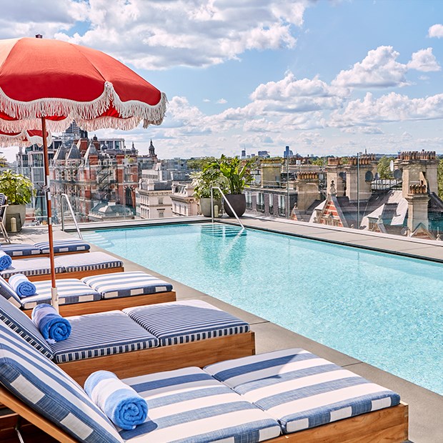 The rooftop pool and bar at The Berkeley with blue and white striped sun loungers, shaders and a view on Hyde Park and the London rooftops