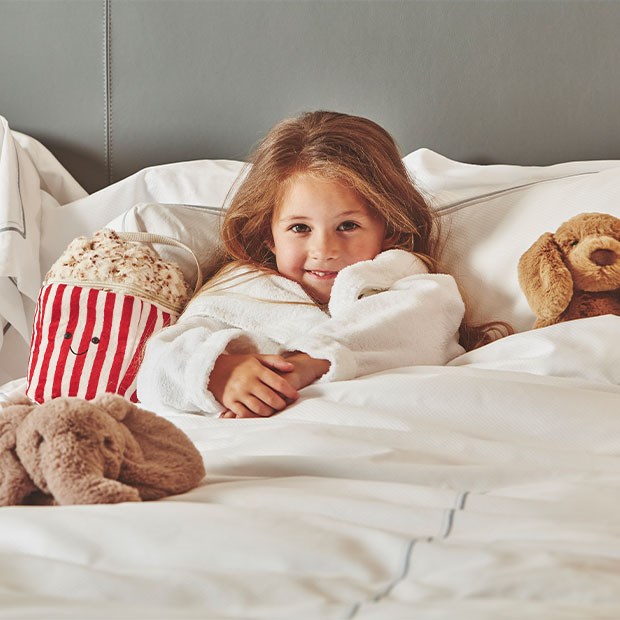Little girl in Berkeley dressing gown under the covers with jellycat toys ad popcorn