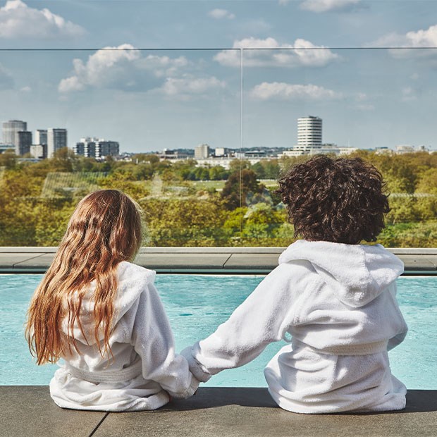 Two children in Berkeley dressing gowns holding hands by the rooftop pool