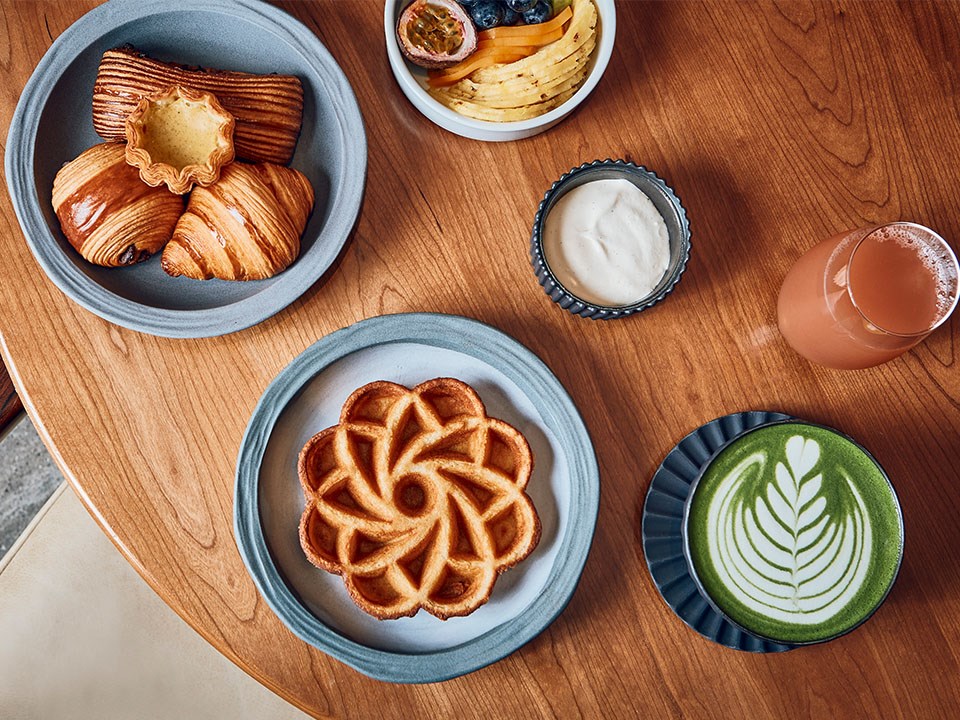 Breakfast selection: pastry basket, flower shaped cake, chopped fruit bowl, matcha latte and a glass of juice