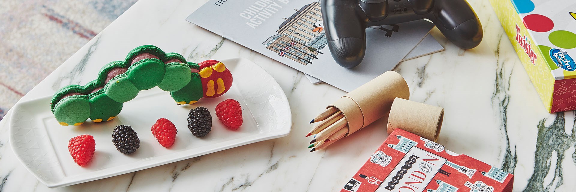 Caterpillar made from macarons, colouring pencils, game console controller, Children's activity book and twister board game on table