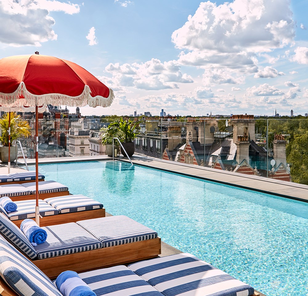 Rooftop pool at The Berkeley with blue and white striped beds and a red umbrella with views of Hyde Park