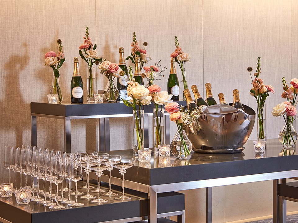 Champagne in ice buckets, champagne glasses and flower on high tables.