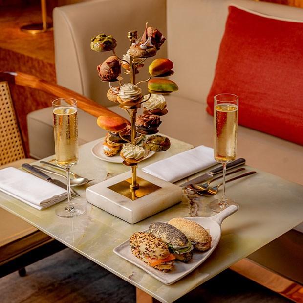 A decadent afternoon tea setup featuring a tiered stand of colorful pastries and macarons, served alongside two glasses of champagne on a luxurious marble table.