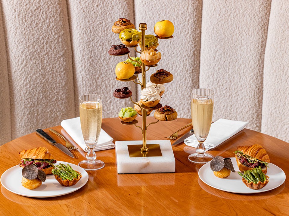 Goutea featuring tiers of Cedric Grolet cakes, savoury selection on plates and 2 glasses of champagne