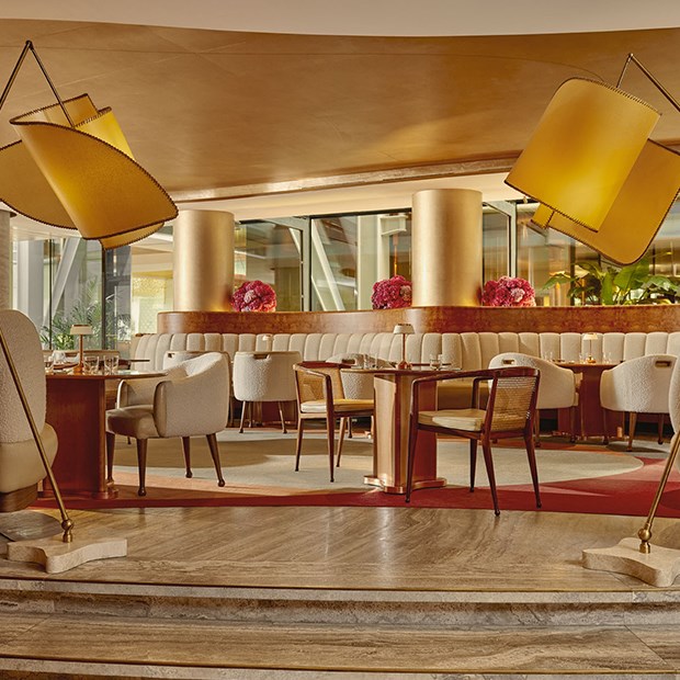 An inviting view of The Berkeley Café’s interior, featuring sculptural gold floor lamps, curved cream seating, and polished wooden tables set for dining.