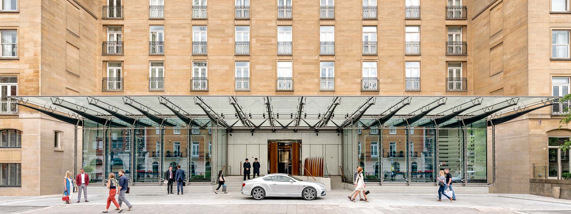 A car in front of the entrance of The Berkeley hotel, as well as passers-by and hotel guests.