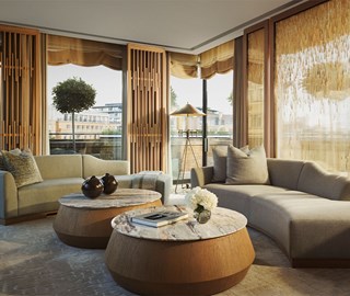 Stylish suite living area with curved grey sofas and two round marble-top coffee tables, set in front of floor-to-ceiling windows with wooden slat accents and sheer drapes, opening to a terrace with potted trees and city views.