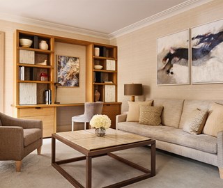 Elegant living room with a beige sofa and armchair surrounding a square coffee table with a marble top, featuring built-in wooden shelving, abstract artwork, and neutral-toned décor for a refined and calming atmosphere.