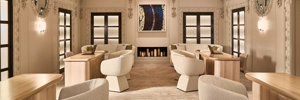 Reception room with curved cream chairs, light wood desks, sofas, and a central fireplace beneath a framed artwork.