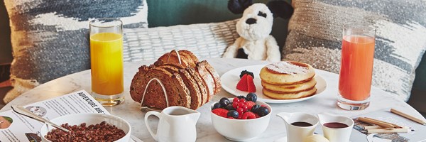 Children's breakfast in suite featuring coco pops, orange juice, toast, berries, pancakes,colouring pencils and jellycat toy dog