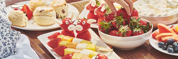 Selection of fruit with scones and cream - little girl picking up a strawberry.