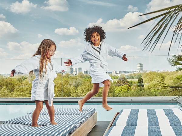2 children in Berkeley dressing gowns jumping from sunbed to sunbed at rooftop pool