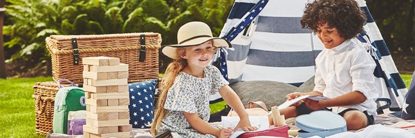 Two children playing in a garden with jenga colouring books, and a blue & white striped teepee