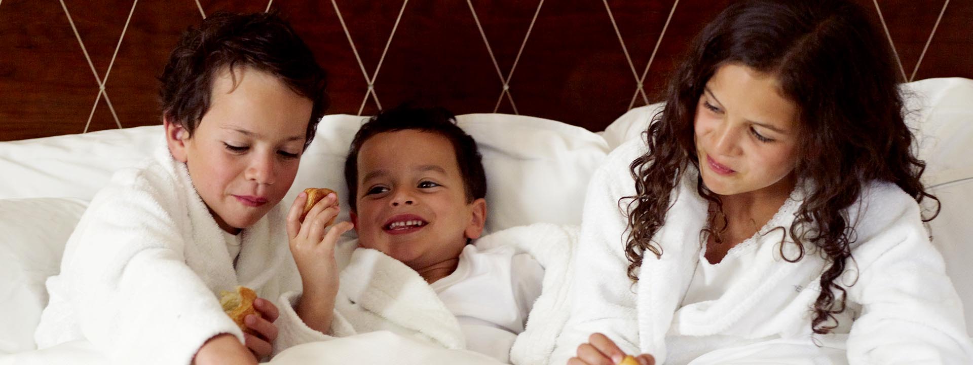 Three happy children smiling and eating at the hotel, in white bathrobes at The Berkeley.