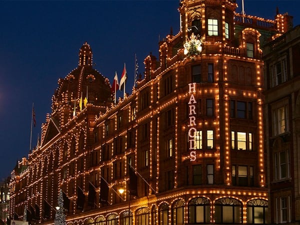 Harrods’ exterior at night, outlined in warm festive lights against a dark sky.
