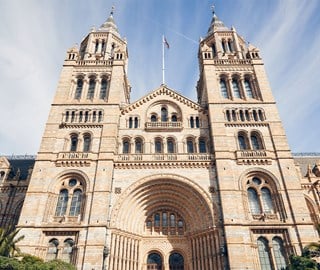 View of the front of the National History Museum, an impressive building with blue sky in the background.