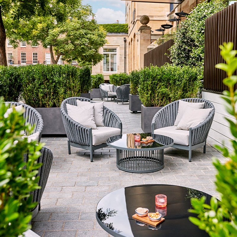 The terrace at The Berkeley Bar & Terrace, with grey outdoor chairs and tables, and greenery around.
