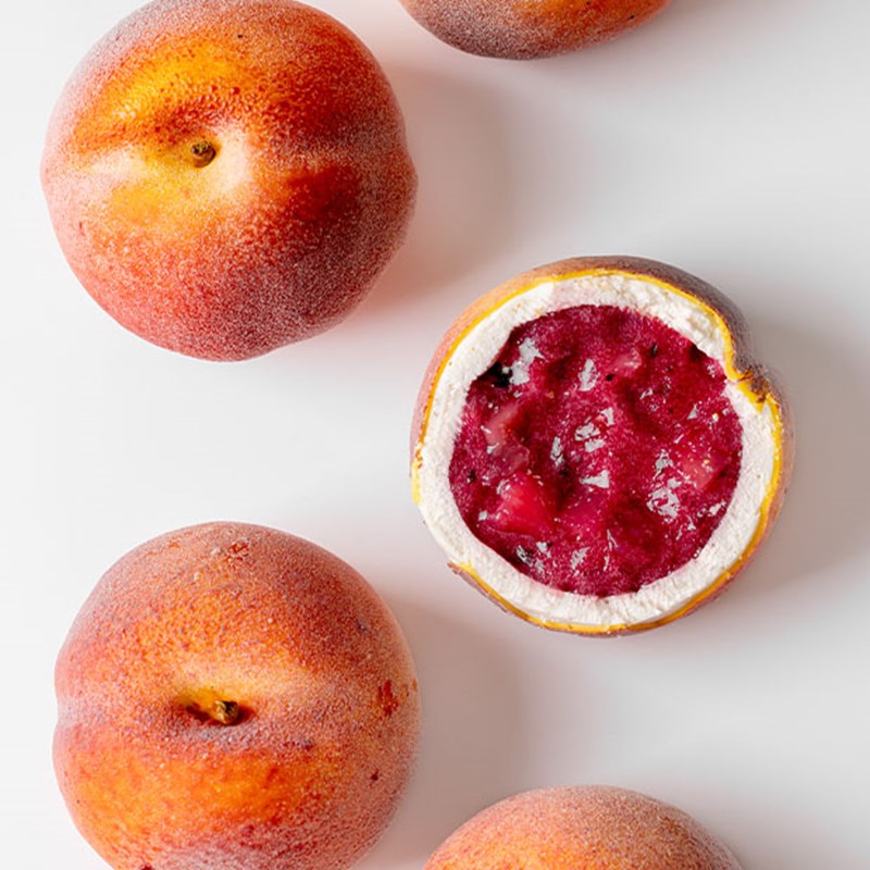A selection of Cedric Grolet cakes that resemble peaches. one of them is cut in half and the cross-section is in view.