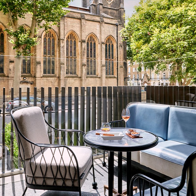 The Berkeley Bar and Terrace: a table with a glass of whisky, wine glass with rose, bar snacks and a cigar resting on an ash tray. Behind is a view of the church across the road.