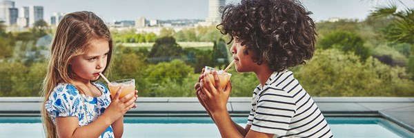 2 children at The Berkeley Rooftop pool, girl on the left and boy on the right, sipping on a drink facing each other.