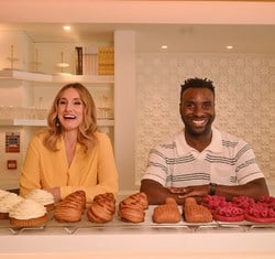 Grace Dent on the left and Jimi Famurewa on the right, smiling stood behind a selection of pastries and cakes by Cedric Grolet