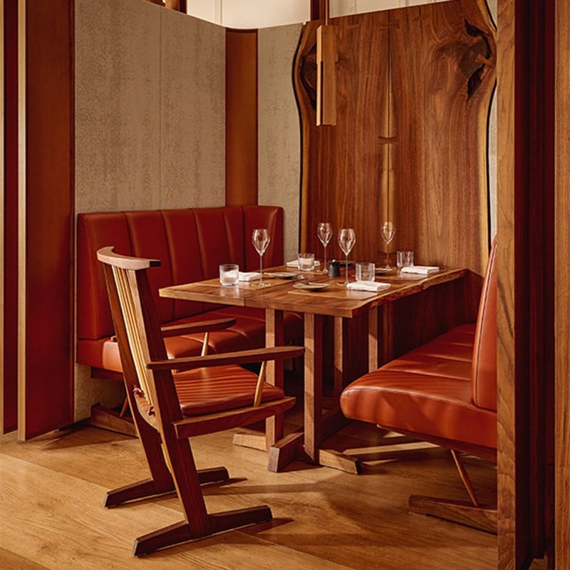 An intimate restaurant booth with warm wood furnishings, red leather seating, elegant table settings, and ambient lighting for a cosy atmosphere.