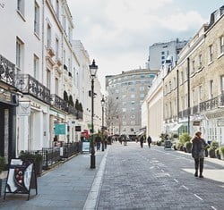 View onto Motcomb street with cobbled pavement and rows of shops.