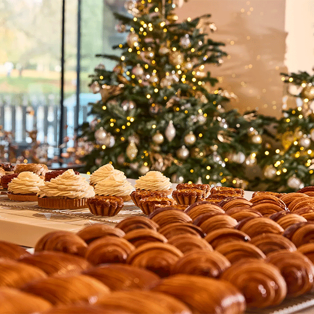 Festive pastry display with croissants and cream-topped desserts set before a decorated Christmas tree.