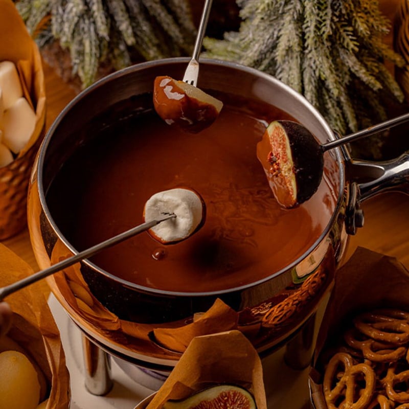 A decadent chocolate fondue set, with skewers holding marshmallows, figs, and fruit ready to dip, surrounded by an assortment of treats for a delightful winter indulgence.