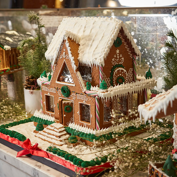 An intricately decorated gingerbread house with green and white icing, candy cane accents, and delicate piping details, evoking a whimsical holiday charm.