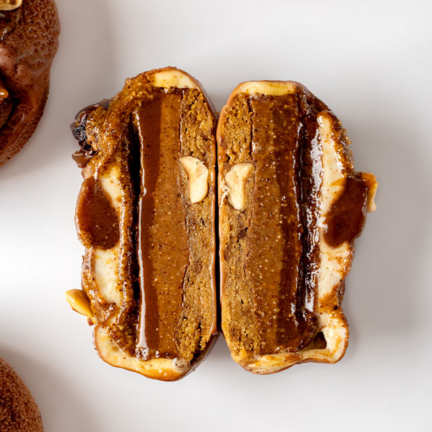 A cross-section of a richly layered pastry, revealing dense caramel and chocolate layers, hazelnuts, and a creamy outer shell, highlighting intricate textures and mouth-watering details.