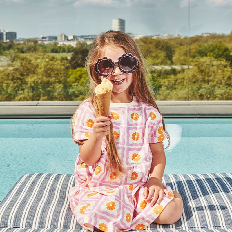 Girl in pink dress and sunglasses with ice-cream on rooftop pool