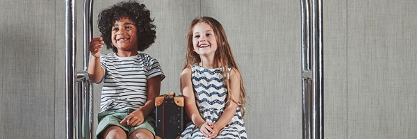 Boy and girl laughing sitting on The Berkeley's luggage trolley with mini suitcases