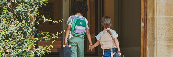 Back view of boy and girl holding hands wearing mini rucksacks