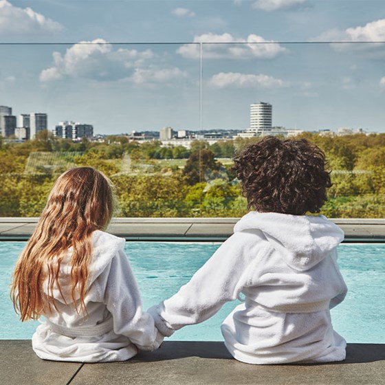 Boy and girl in The Berkeley's white dressing gowns holding hands by the Berkeley rooftop pool