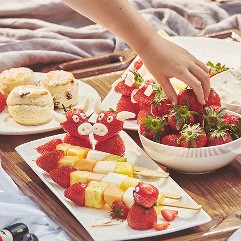 Scones, fruit selection, cream and girl's hand picking up a strawberry.