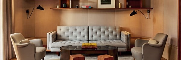Elegant hotel lounge with a grey sofa, armchairs, modern coffee table, and wall shelving.