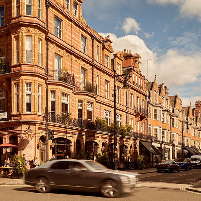 Red-brick townhouse buildings in Mayfair with shops, restaurants, and a passing car.