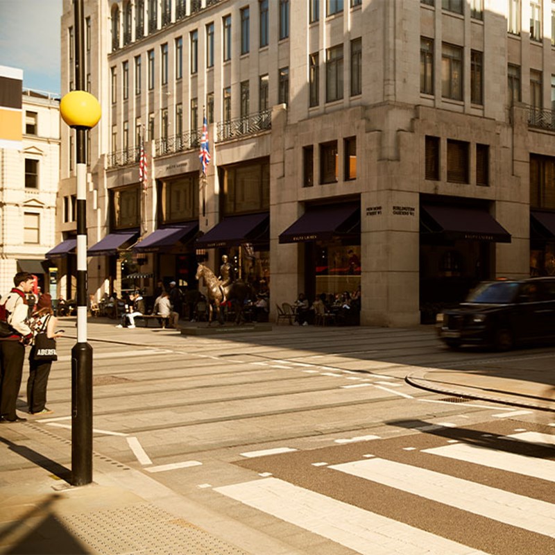 Street corner view with Ralph Lauren store, people crossing at a zebra crossing, and UK flags above.
