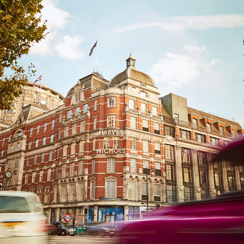 Historic Harvey Nichols building with red and white façade, cars passing, and a London Underground sign.