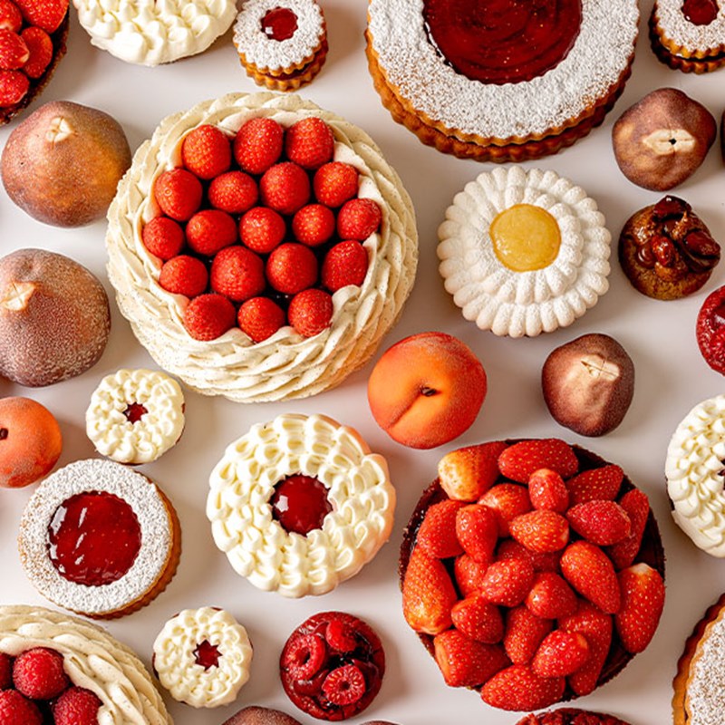 Assorted pastries and desserts decorated with strawberries, cream, and fruit arranged on a table.