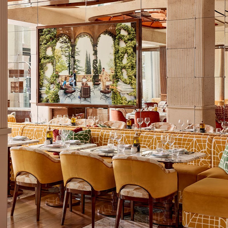 Stylish restaurant interior with patterned banquettes, yellow chairs, and a large wall artwork.
