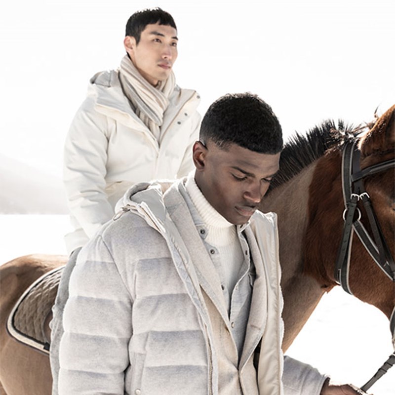 two men in eleventy beige coloured coats,  with one leading a horse while the other sits astride, both looking into the distance with serious expressions