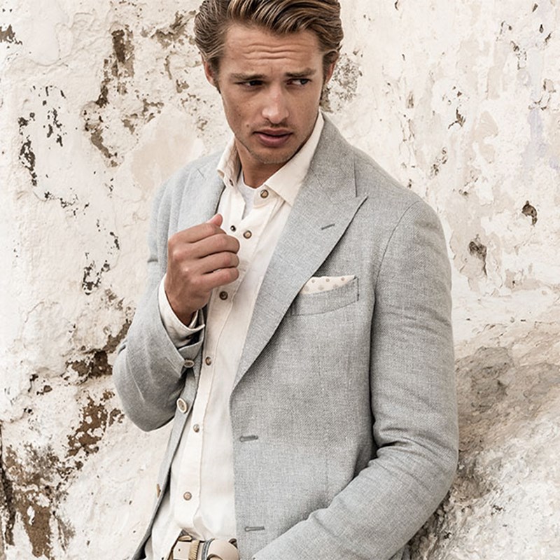 man dressed in eleventy clothing, a grey blazer, white shirt and white pocket square in the blazer.