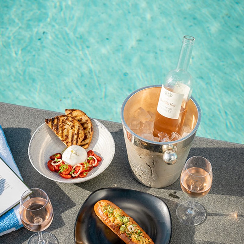 A bottle of chilled wine and a plate of food on the edge of the pool