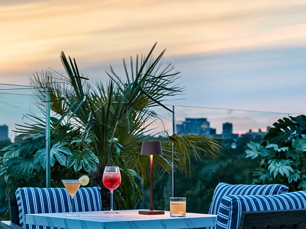 3 different cocktails on a table by the rooftop pool, an evening atmosphere with the sun setting in the background