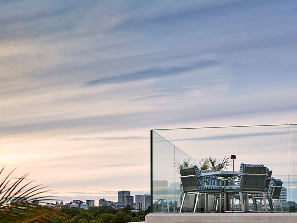 an evening view of the terrace by the rooftop pool, and tall London buildings and a sunset creating the backdrop