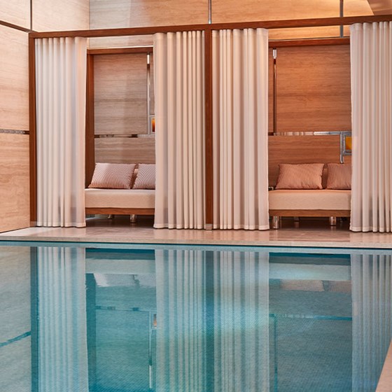 Two day beds dressed with cream linen and flowing drapes next to a swimming pool