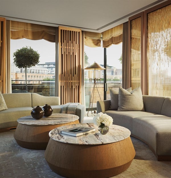 Elegant living room with curved modern sofas, two round marble-top coffee tables, and large windows opening to a terrace with city views, softened by wood paneling and sheer curtains.